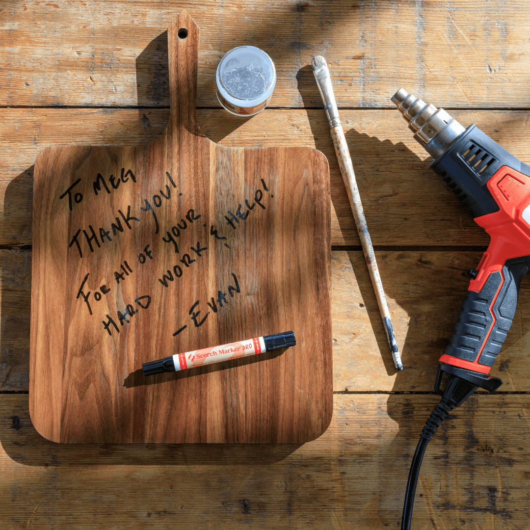 Walnut cutting board on a workbench with a heat gun and Scorch Marker wood burning tools
